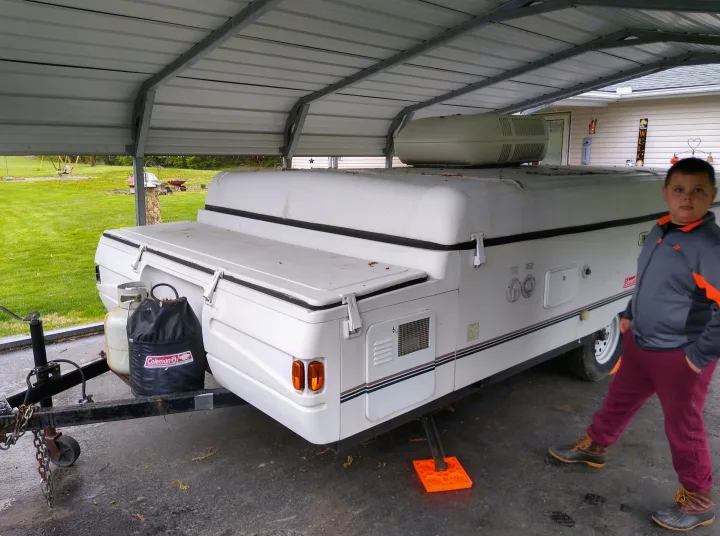 White pop-up RV camper parked under a carport with a boy beside it. Ideal for an RV rental getaway.. Coleman Other 2000