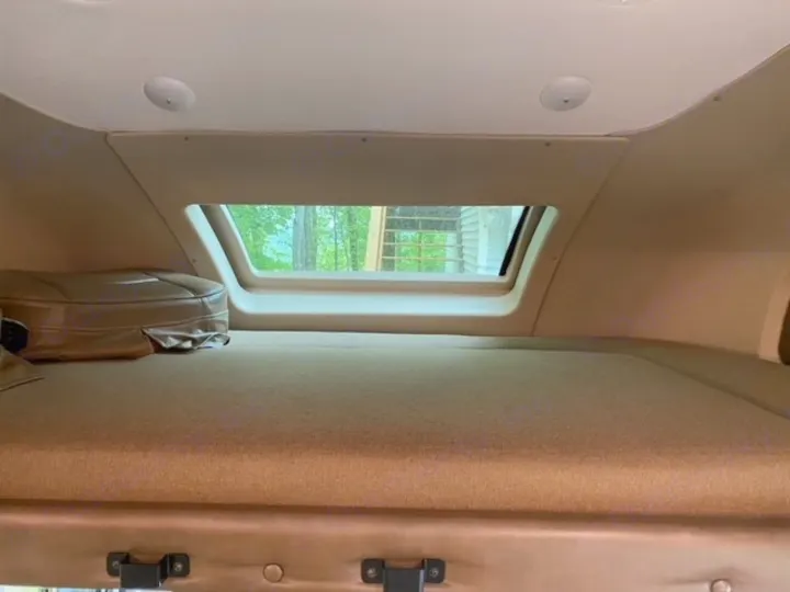 Inside an RV rental: a cozy cab-over bunk bed with a large window view of lush trees, ready for your adventure.. Tiffin Motorhomes Wayfarer 2019