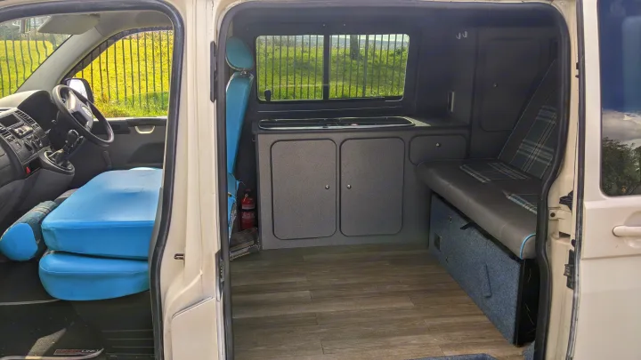 This RV rental's inviting camper van interior features a practical kitchen unit, comfortable seating, and versatile bed setup.. vw T5 2004