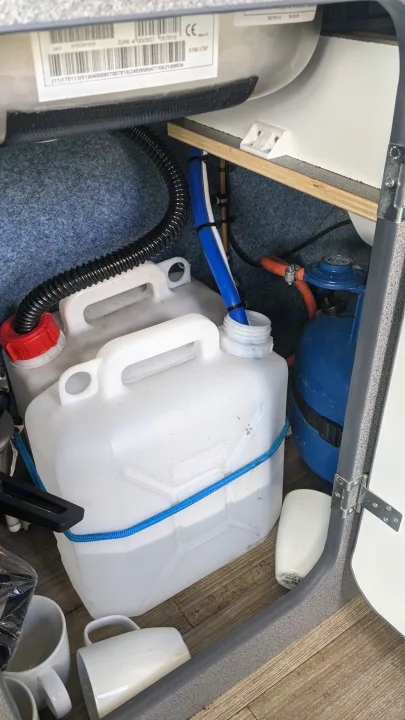 A compact RV rental utility compartment with water jugs, a blue gas system, and various essential plumbing hoses for onboard living.. vw T5 2004