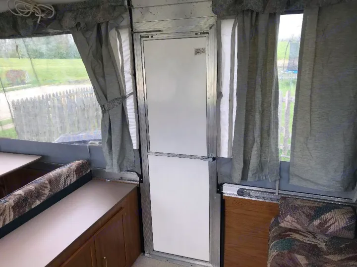 Inside a cozy pop-up camper for your RV rental. Features dinette seating, large windows with curtains, and a split entry door.. Coleman Other 2000