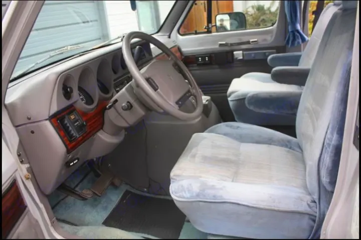 Detailed view of a classic RV rental interior, highlighting the dashboard, steering wheel, and plush blue seating.. Roadtrek 190 Popular 1994