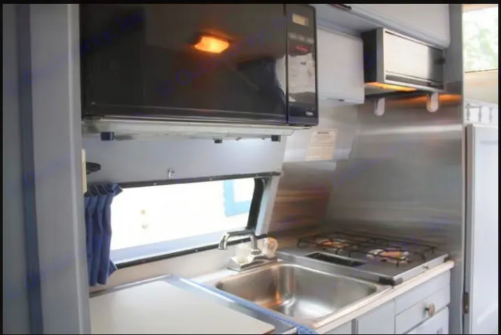 RV rental kitchen interior: black microwave, stainless sink, 2-burner stove, and overhead cabinets.. Roadtrek 190 Popular 1994