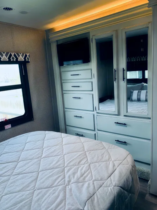 Modern RV rental bedroom featuring a comfy bed, integrated storage unit with TV, and mirrored closet doors. Ideal for travel.. Entegra Coach Odyssey 31F 2021