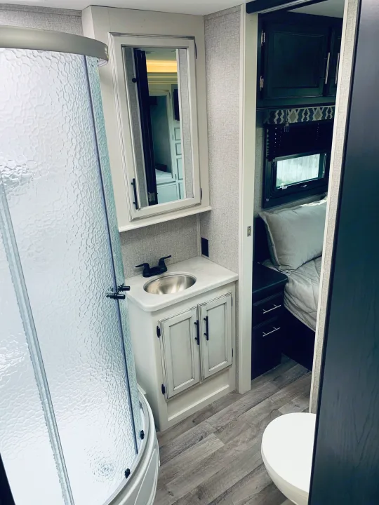 RV rental interior: compact bathroom with shower, vanity, sink, and toilet, leading to a cozy bedroom area.. Entegra Coach Odyssey 31F 2021