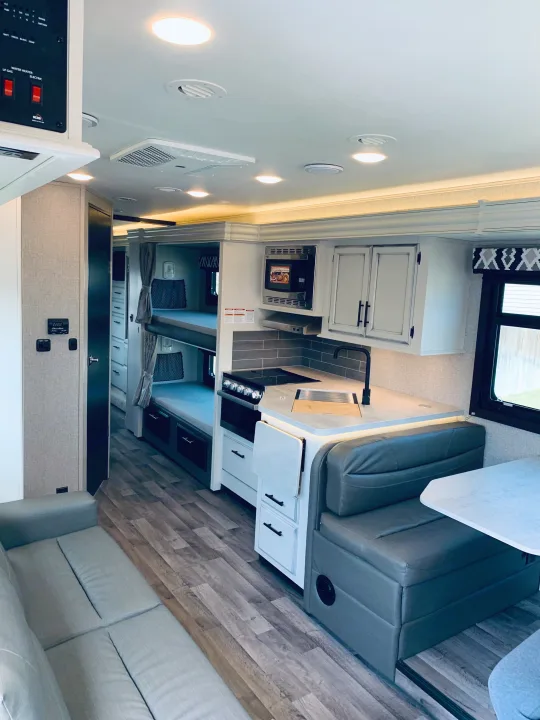 Bright RV rental interior showcasing a modern kitchen, dining booth, sofa, and bunk beds. Ideal for adventures.. Entegra Coach Odyssey 31F 2021