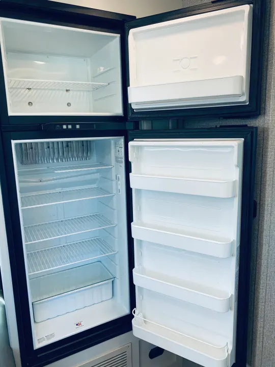 Inside an empty, clean RV refrigerator, ready for your next rv rental. Top freezer, bottom fridge, prepped for your journey.. Entegra Coach Odyssey 31F 2021