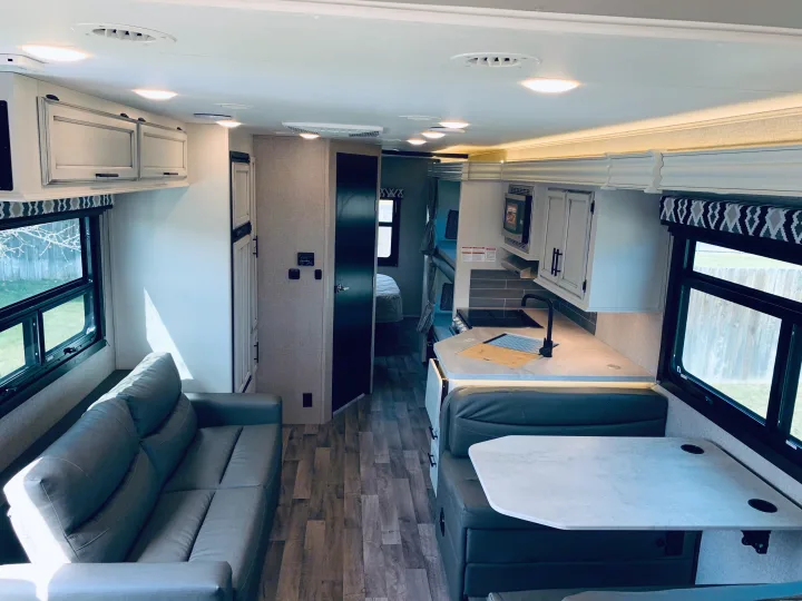 View inside an RV rental, highlighting its bright, modern living room, kitchen, and dining area.. Entegra Coach Odyssey 31F 2021