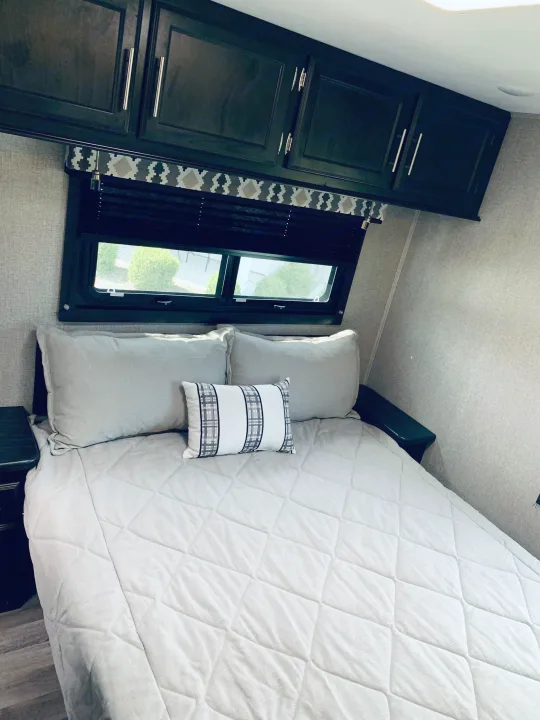 Comfortable RV rental bedroom featuring a quilted bed, overhead storage cabinets, and a bright window.. Entegra Coach Odyssey 31F 2021