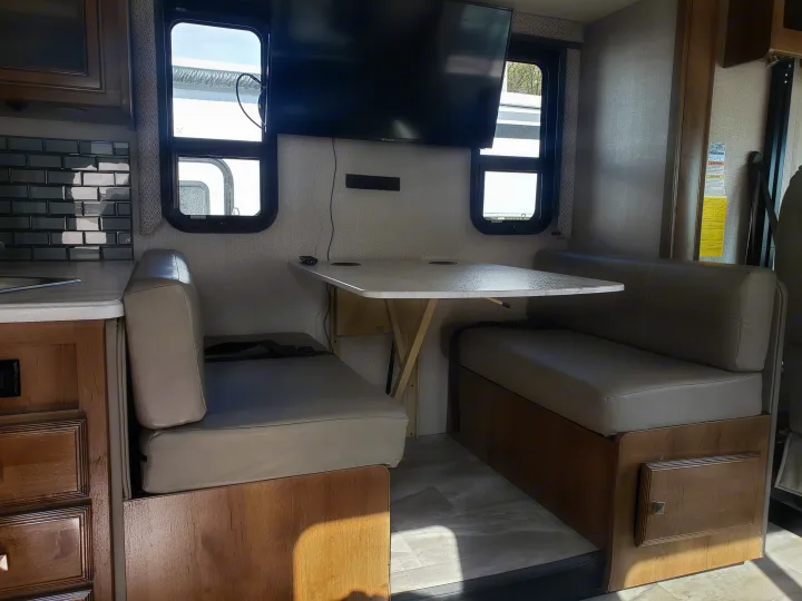 Step inside this RV rental's dinette: light-colored upholstered bench seats, a white foldable table, and wall-mounted TV.. Holiday Rambler Admiral 2021