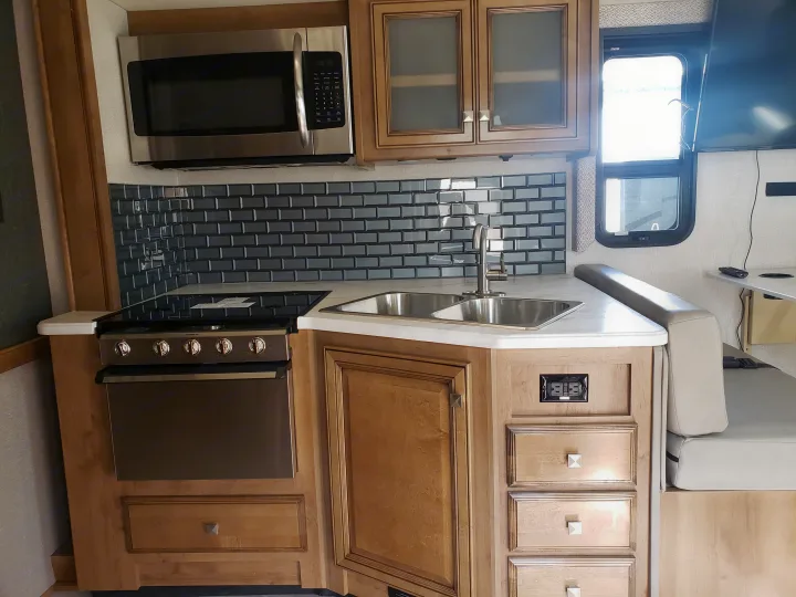 Compact RV rental kitchen: stainless steel appliances, double sink, dark subway tile backsplash, and light wood cabinetry.. Holiday Rambler Admiral 2021