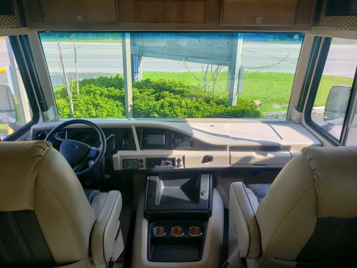Inside an RV rental: View from front seats, showing dashboard, steering wheel, and road through the windshield.. Holiday Rambler Admiral 2021