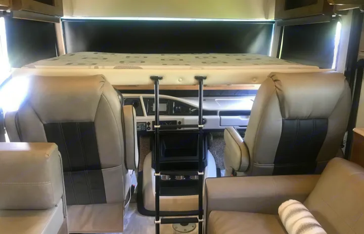 Inside a modern RV rental: overhead bunk, driver & passenger captain's chairs, and front dashboard. Perfect for travel.. Holiday Rambler Admiral 2021
