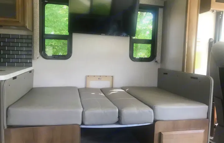 RV rental: Dinette converted to a bed with light gray cushions, dual windows, and a wall-mounted TV for compact comfort.. Holiday Rambler Admiral 2021