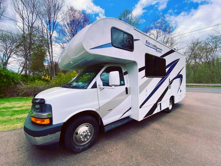 Hit the road in this white rv rental with black & blue graphics. Parked outdoors under blue sky, ready for your next adventure!. Thor Freedom Elite 2021