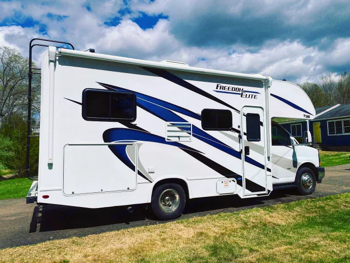 A white Freedom Elite RV with blue graphics is parked, ready for your next rv rental adventure or camping trip.. Thor Freedom Elite 2021