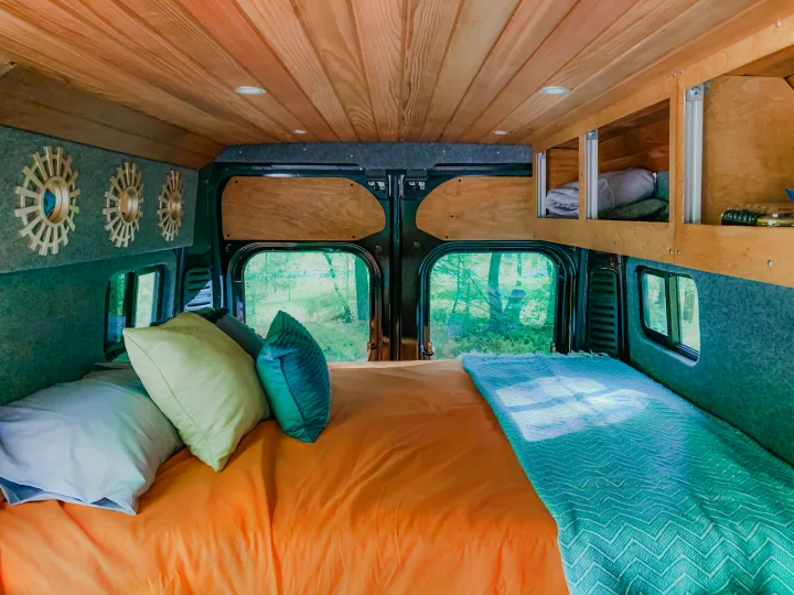 RV rental van interior features a comfy bed, wood ceiling, custom storage, and scenic views out the rear windows.. Ram Promaster 1500 2021