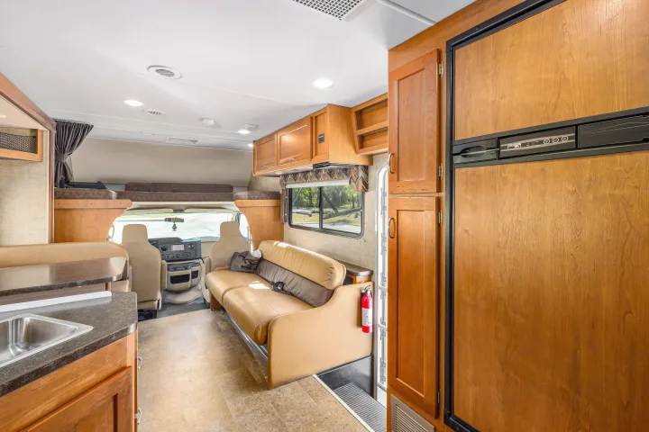 Bright RV rental interior featuring a comfy sofa, kitchen with sink & fridge, and bunk bed above the cab.. Winnebago Spirit 2017