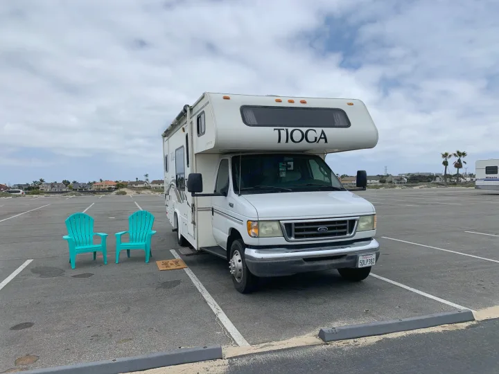 White Tioga RV rental with turquoise chairs in a large parking lot, ready for an outdoor adventure.. Fleetwood Tioga 2003