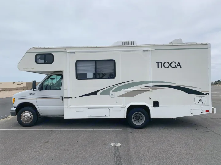 White Tioga RV rental, side view, parked on asphalt. This motorhome is ready for beach camping adventures.. Fleetwood Tioga 2003