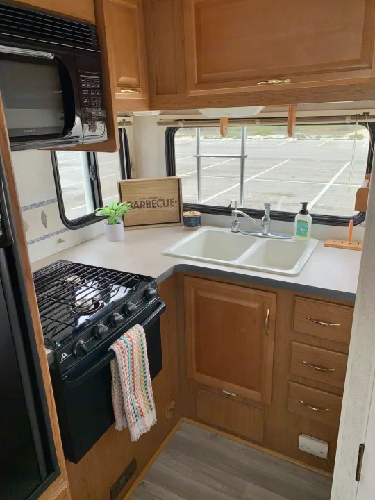 Explore this cozy RV rental kitchen with a microwave, gas stove, dual sink, and storage, ideal for road trips.. Fleetwood Tioga 2003
