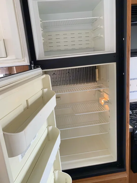 Clean, empty RV rental refrigerator, top freezer. Open doors reveal wire shelves & door bins. Light is on.. Fleetwood Tioga 2003