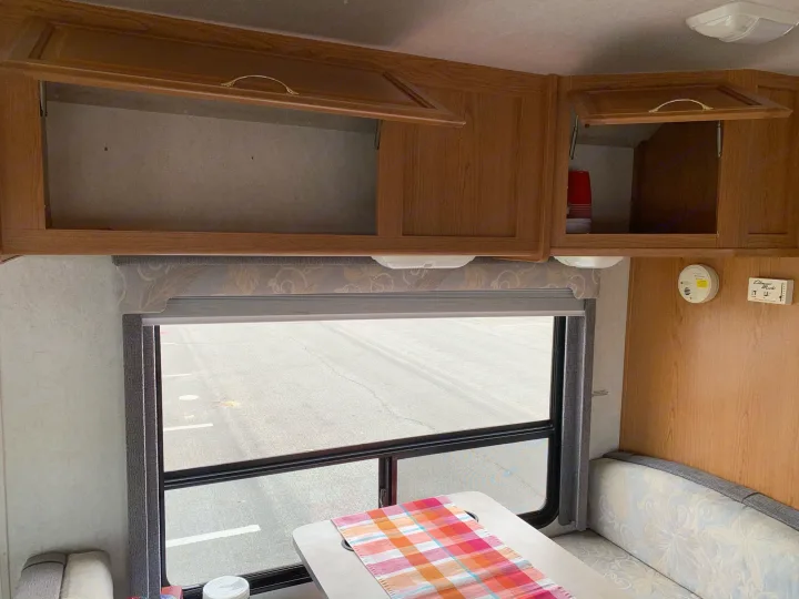 RV rental interior: Open wooden cabinets, a dinette with a plaid runner, and a window view of asphalt.. Fleetwood Tioga 2003