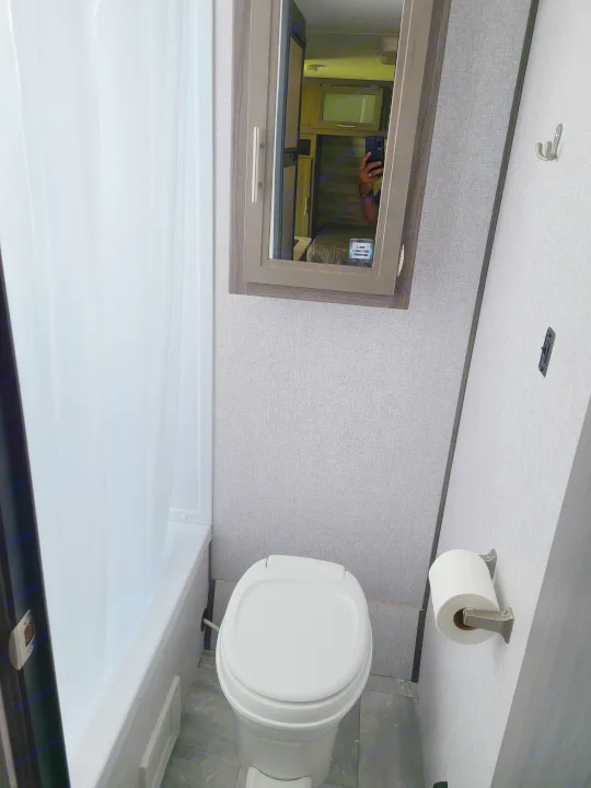 Compact RV rental bathroom features a toilet, shower with curtain, and mirrored medicine cabinet. Functional and efficient space.. Dutchmen Kodiak 2021