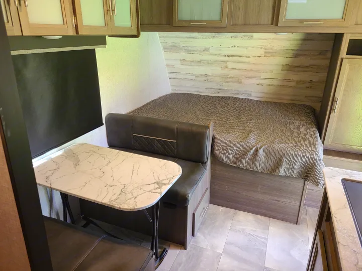 RV rental interior: a comfortable dinette with a marble-patterned table, adjacent to a bed with a striped comforter.. Dutchmen Kodiak 2021