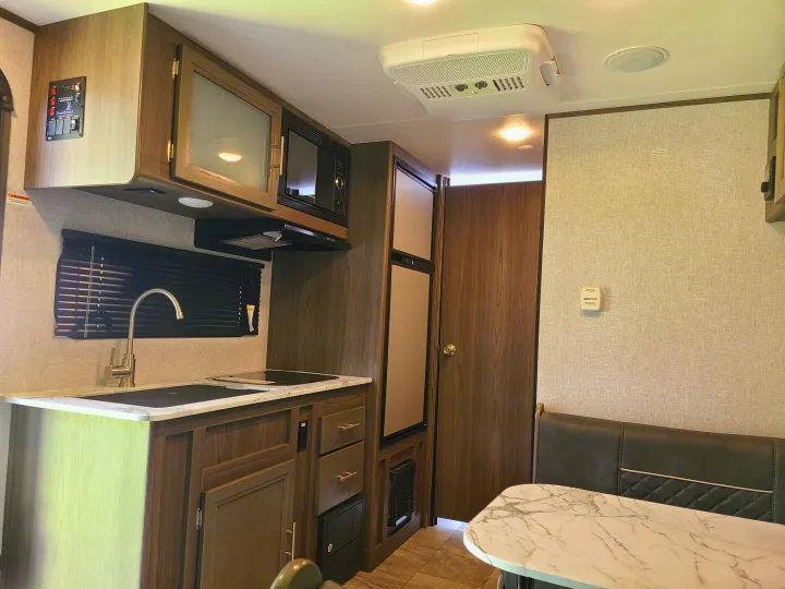 RV rental kitchen & dining area: sink, stovetop, microwave, fridge, AC unit, and comfy dinette.. Dutchmen Kodiak 2021
