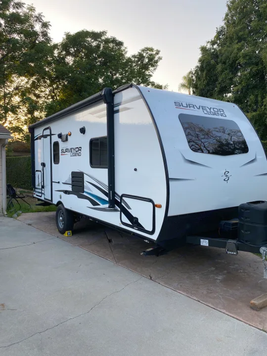 A white Surveyor Legend travel trailer, ideal for your next RV rental adventure, is parked on a concrete driveway.. Forest River Surveyor 2021