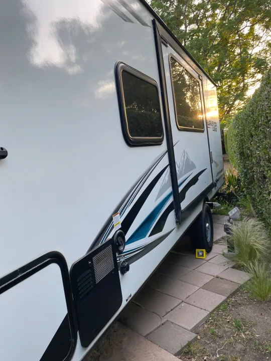 Side view of a white Surveyor Legend travel trailer, ready for an RV rental. Parked on pavers, showing windows and graphics.. Forest River Surveyor 2021