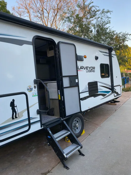 A white Surveyor Legend travel trailer, a great RV rental option, parked with its entry steps deployed, ready for an adventure.. Forest River Surveyor 2021