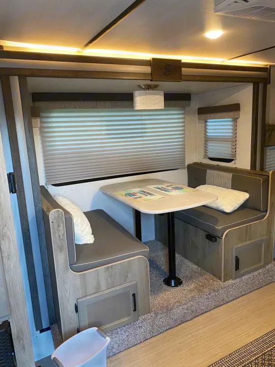 Modern RV rental dinette with cozy bench seating, ideal for travel. Features light wood accents and window blinds.. Forest River Surveyor 2021