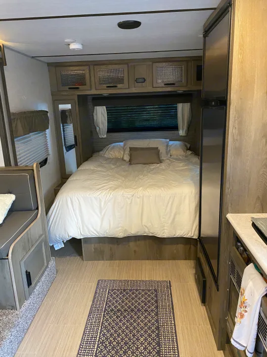 Inside a modern RV rental: a plush queen bed, overhead storage, fridge, and dinette. A cozy home on wheels awaits.. Forest River Surveyor 2021