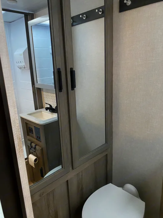 This compact RV rental bathroom features a toilet, sink, mirrored cabinet, shower, and useful wall hooks.. Forest River Surveyor 2021