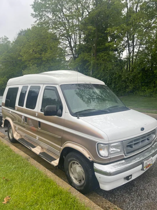 White and gold Ford conversion van, perfect for an RV rental. Parked curbside on a rainy day.. Coachmen Van Conversion 2001