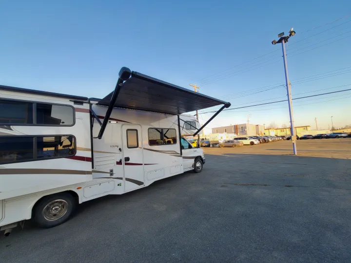 White motorhome RV rental parked on an asphalt lot with its black awning extended under a clear blue sky.. Forest River Sunseeker 2018