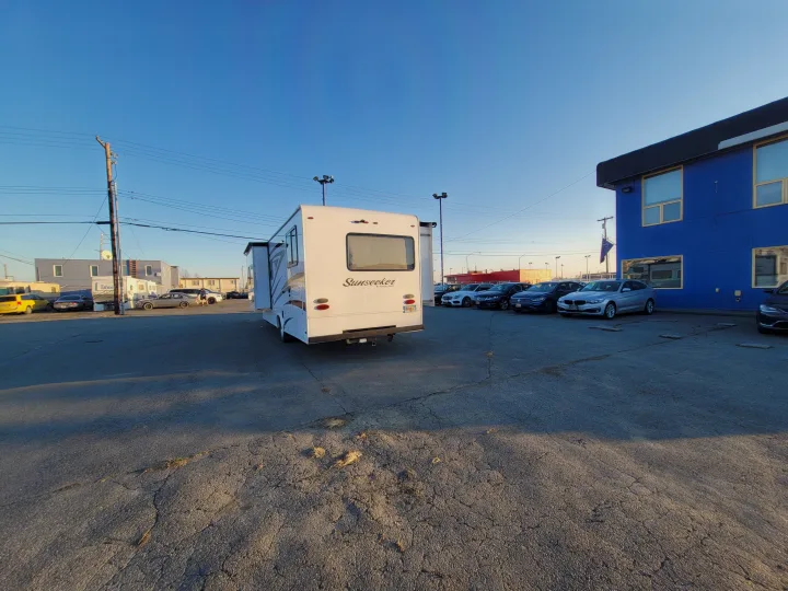 White Sunseeker RV in a parking lot, ready for RV rental. Other vehicles and a blue building are visible under a clear sky.. Forest River Sunseeker 2018