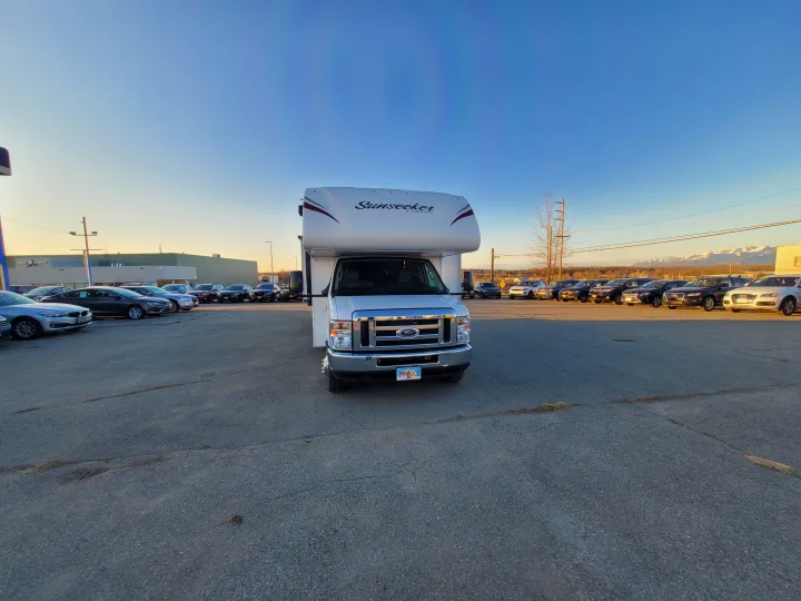 White Sunseeker rv rental, a Ford Class C, parked in an Alaska dealership lot with distant snow-capped mountains under a clear sky.. Forest River Sunseeker 2018