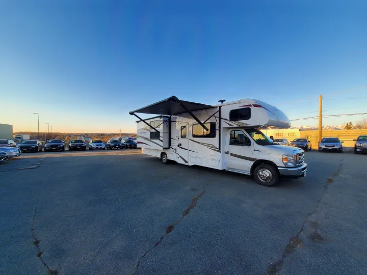 Spacious white RV rental with awning extended, parked in a lot under a clear sky, ready for outdoor adventures and travel.. Forest River Sunseeker 2018