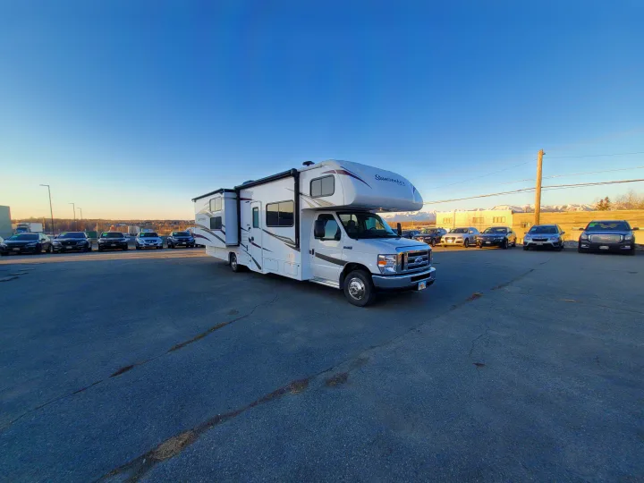 White Sunseeker Class C RV rental on an asphalt lot, with extended slide-outs and distant mountains.. Forest River Sunseeker 2018