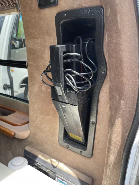 RV rental: Built-in wall compartment holding a portable vacuum cleaner with tangled cords, typical RV storage solution.. Coachmen Van Conversion 2001