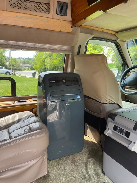 Inside an RV rental van with a portable LG AC unit, cooler, and comfortable seating, ideal for travel.. Coachmen Van Conversion 2001