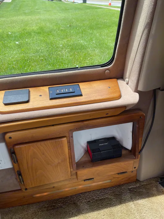 RV rental interior with USB charging ports, power inverter (BESTEK 300W), and wooden cabinetry. View of grass outside.. Coachmen Van Conversion 2001