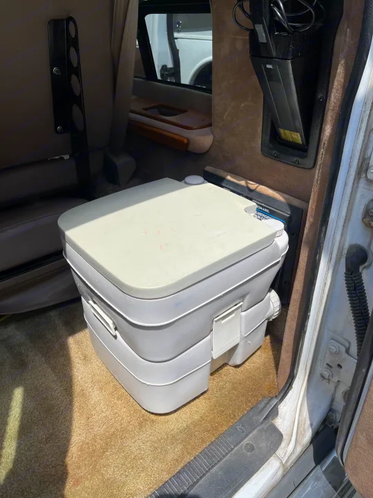 A compact, white portable toilet sits on the beige carpet of an RV rental, ready for convenient travel.. Coachmen Van Conversion 2001