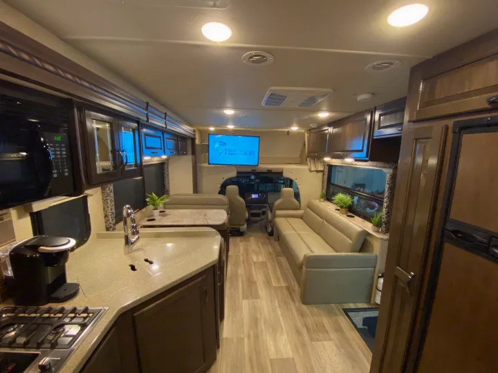 Inside a well-appointed RV rental, showing a kitchen with a sink and stove, dining booth, and living room sofa. Ideal for travel.. Thor Motor Coach Four Winds with full wall slide 2018