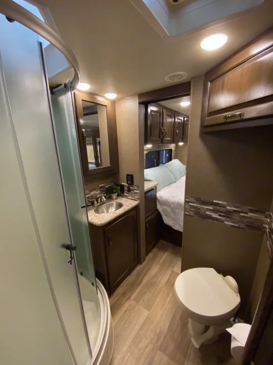 RV rental interior: A well-appointed bathroom with shower, sink, and toilet, leading to a comfortable bedroom area.. Thor Motor Coach Four Winds with full wall slide 2018