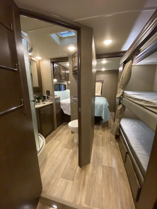 RV rental interior: full bath (shower, toilet, sink), main bed, and bunk beds. Compact, modern living space for travel.. Thor Motor Coach Four Winds with full wall slide 2018