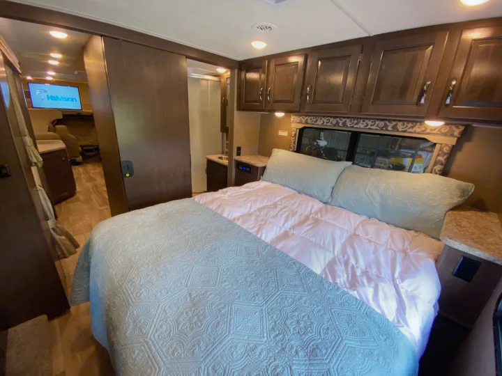 Cozy RV rental interior: main bedroom with quilted bed, built-in cabinets, and a hall to the living area w/ TV.. Thor Motor Coach Four Winds with full wall slide 2018